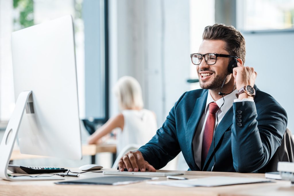 selective focus of happy businessman in headset smiling in office